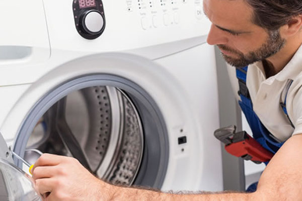 Appliance repair technician from Hudson Appliance Repair & Removal working on a coin-operated washing machine in shared laundry room